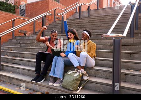 Diverse university students celebrating academic success on campus stairs Stock Photo