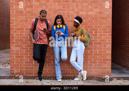 Diverse students using smart phones against brick wall Stock Photo