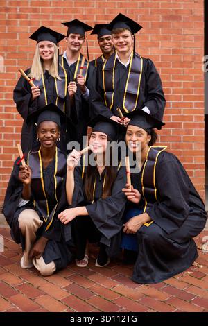 Diverse students celebrating graduation, holding diplomas and smiling Stock Photo