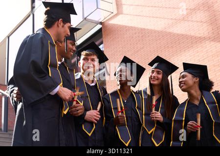 Diverse students celebrating graduation, holding diplomas, and smiling Stock Photo