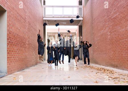 Graduating students jumping and throwing caps in air Stock Photo
