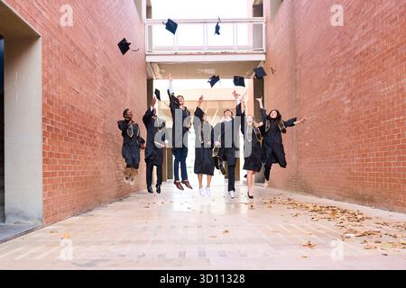 Diverse students celebrating graduation, jumping and throwing mortarboards Stock Photo