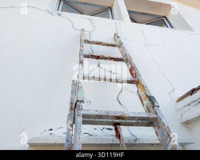 Builder's ladder propped against side of a house to repair cracks in the wall Stock Photo