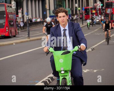 Office worker commuter riding across London Bridge on a hired electric Lime bike, England, UK Stock Photo