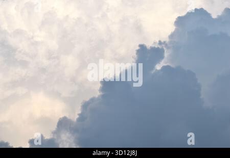 A dramatic diagonal contrast between a heavy, dark grey storm cloud and a bright, ethereal mass of sunlit white clouds, creating an abstract and moody Stock Photo