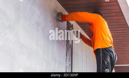Worker applying Conwood adhesive on the wall, an essential step in installing decorative material made from cement and wood fibers. Stock Photo