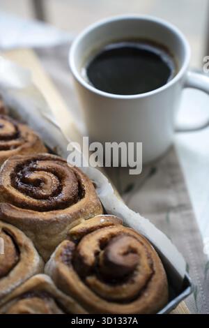 Freshly baked cinnamon rolls on a wooden board with a cup of coffee Stock Photo