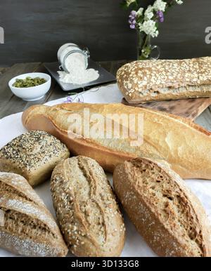 Various freshly baked artisanal breads and rolls presented on a white cloth on a rustic wooden table Stock Photo