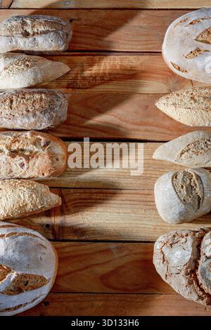 Various types of fresh artisanal bread, including baguettes and round loaves, arranged on a rustic wooden table Stock Photo