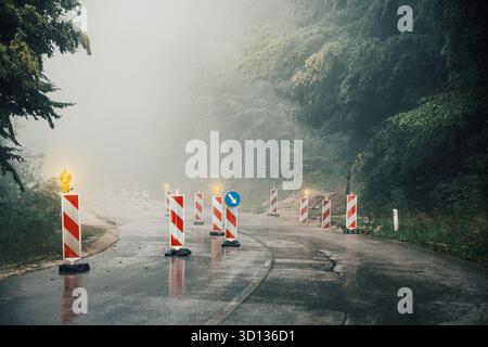 Construction barriers limiting access on a wet mountain road shrouded in thick fog, creating a moody and dangerous atmosphere Stock Photo