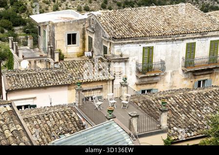 Ragusa, Sizilien - Italy - 04-03-2025: Aerial view of rooftops in Ragusa, with terracotta tiles, green shutters, and a terrace with chairs, typical of Stock Photo