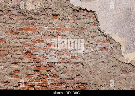 Old brick wall with aged orange blocks and crumbling gray plaster showing damaged facade creating a textured background Stock Photo