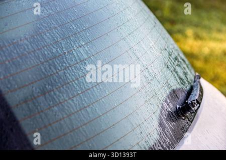 Car rear window covered with rain drops and defroster lines. Wiper resting on wet glass Stock Photo
