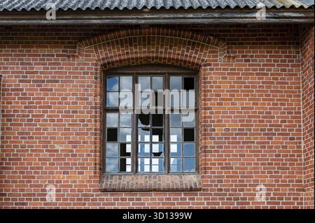 An old window with broken glass panes in a red brick wall. Close-up Stock Photo