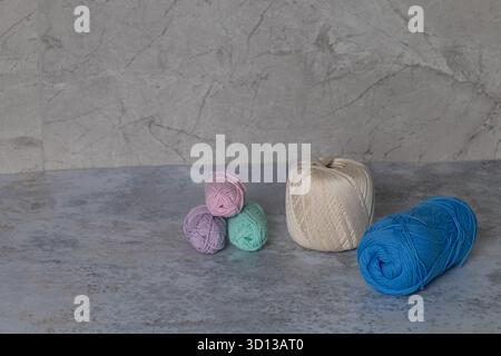Colorful yarn balls in shades of blue, green, pink, and white, arranged on a textured gray surface, highlighting the beauty of crafting materials Stock Photo