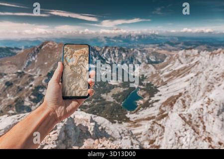 Person navigating mountain peaks and valleys using a smartphone app while hiking, showing concept of outdoor technology Stock Photo