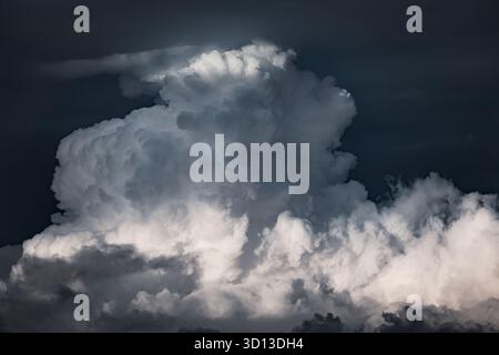 Large cumulonimbus cloud building in a dark sky. Sunlight illuminating parts of the cloud while others remain deep in shadow Stock Photo