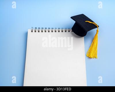 White blank notebook with black graduation cap on blue background. Concept for education planning, study goals, to-do list for students, congratulatio Stock Photo
