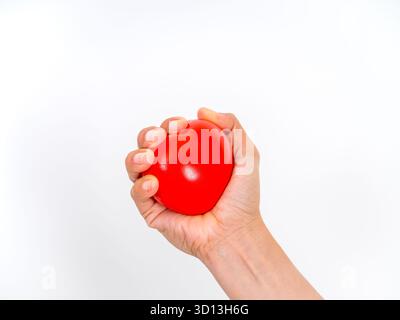 Hand squeezing a red heart-shaped stress ball, symbolizing heart health, blood pressure monitoring, stress relief, cardiovascular care, and medical we Stock Photo