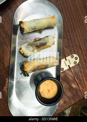 Three fried asian spring rolls with dipping sauce on a metal serving tray Stock Photo