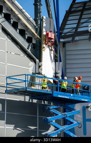 Workers on an access platform fitting a cladding slab using a suction cup lifter on a crane.  Etihad North Stand expansion, Manchester, England, UK. Stock Photo