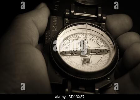Compass in hand. Search for direction and purpose. Image of a hand holding a compass, in dark tones, with tinting. Finding a way and overcoming diffic Stock Photo