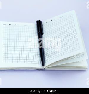 An open notebook with a black pen resting on a blank page. Notebook features grid paper and is placed on a light purple background Stock Photo