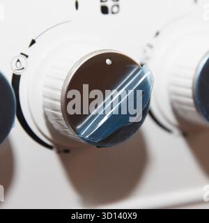 Close-up of appliance control knobs, gas stove. Three round knobs with white bases and dark tops, covered with protective film. On middle handle, prot Stock Photo