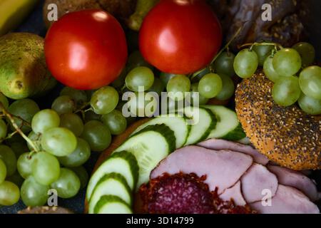 A rich still life of ham, salami, tomatoes, cinnamon buns, bananas, pears, and grapes arranged in studio lighting. Perfect for food advertising or res Stock Photo