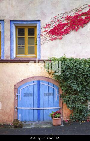 Farbenfrohe Hausfassade mit blauem Holztor, Fenster, Efeu Stock Photo