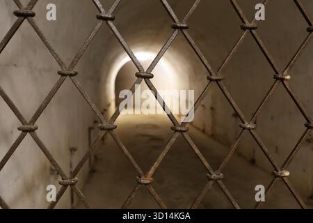 Rusty metal grid in front of dimly lit underground tunnel with arched exit Stock Photo