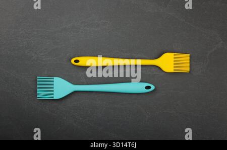 Two silicone brushes for pastry or basting on black slate board with copy space, colorful modern culinary kitchen utensils, close up, elevated table top view, directly above Stock Photo