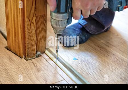 The master screws the thresholds in the doorway on the laminate floor, hands close-up Stock Photo