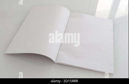 Blank pages of a large grid paper notebook, lying open on a reflective white table surface, offer ample copy space, symbolizing new ideas, learning, and fresh beginnings Stock Photo