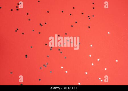 Glittering star-shaped confetti on a red background. Festive holiday celebration concept. Top view. Stock Photo