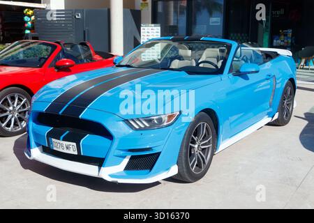 Bright blue convertible Ford Mustang sports car with black racing stripes parked in front of a modern showroom on a sunny day Stock Photo