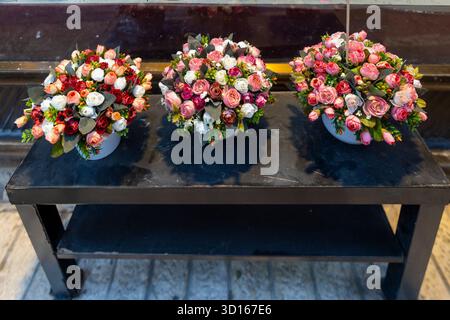 A series of three tightly arranged floral arrangements, featuring a mix of pink, red, and white roses, sit on a dark, rustic display table outdoors on Stock Photo