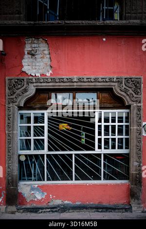 Weathered red building wall with ornate stone window frame and barred metal grille in a traditional architectural style Stock Photo