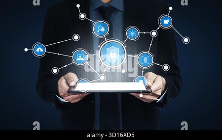 A businessman holds a tablet displaying digital icons connected by lines, symbolizing innovation, connectivity, and modern technology in a secure envi Stock Photo