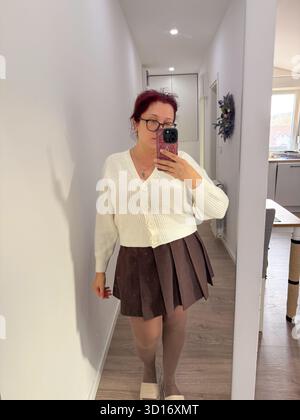 Woman in white cardigan and brown skirt taking mirror photo. Light tones, home interior, and balance of color and texture. Stock Photo