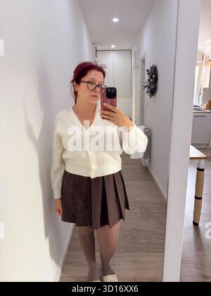 Woman in white cardigan and brown skirt taking mirror photo. Light tones, home interior, and balance of color and texture. Stock Photo