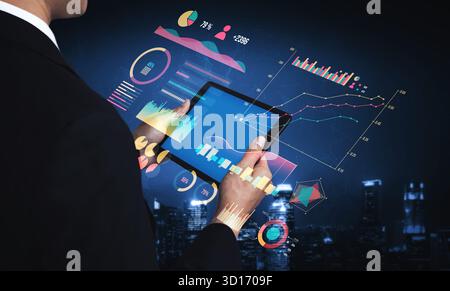 A businessman engages with a tablet displaying vibrant data visualizations and graphs in a stylish urban environment at night. Impute Stock Photo