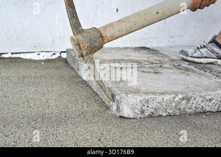Installing new pavement or floor outside from large concrete tiles, closeup detail on worker fitting stone block over sand and gravel base layer using Stock Photo