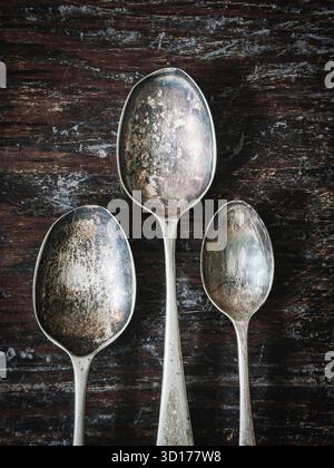 Three old tarnished spoons on wooden background. Stock Photo