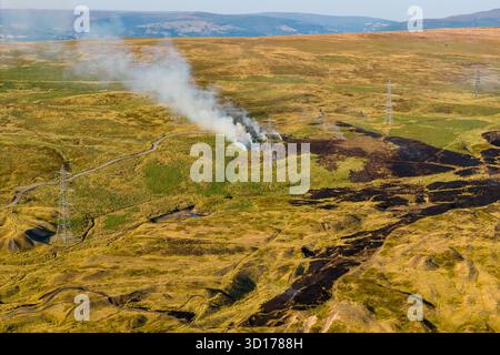 Aerial drone view of a grass and moorland fire smoking near electricity pylons in Wales Stock Photo