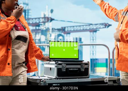 Green screen laptop used by offshore rig technicians monitoring operations on oil platform deck. Teamworking drilling rig colleagues reviewing energy operations using mockup notebook, close up Stock Photo