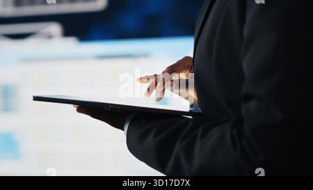 Close up of businesswoman using tablet to compare company KPIs data on digital videowall before making decisions. Entrepreneur analyzing key performance indicators using device app Stock Photo