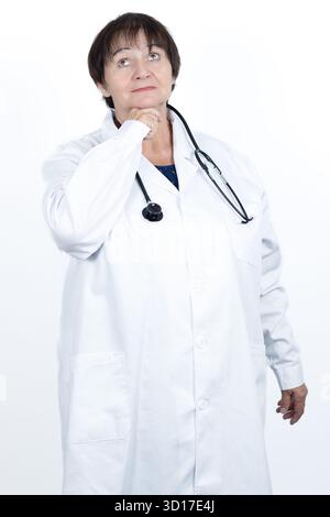 Mature female doctor in a white lab coat and stethoscope thinking, looking up with a pensive expression, representing medical expertise Stock Photo