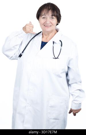 Senior woman doctor in lab coat with stethoscope, smiling and making a call me hand gesture, friendly and confident, suggesting communication Stock Photo