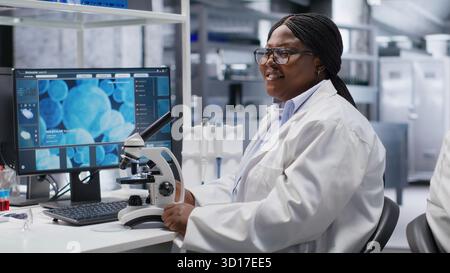 African american chemist analyzing molecular samples in a lab, using professional microscope. Healthcare innovation and biochemistry experiments represent scientific method and discovery. Stock Photo
